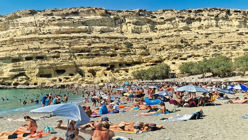 zatłoczona plaża ze skałami z jaskiniami w tle w Matala na Krecie